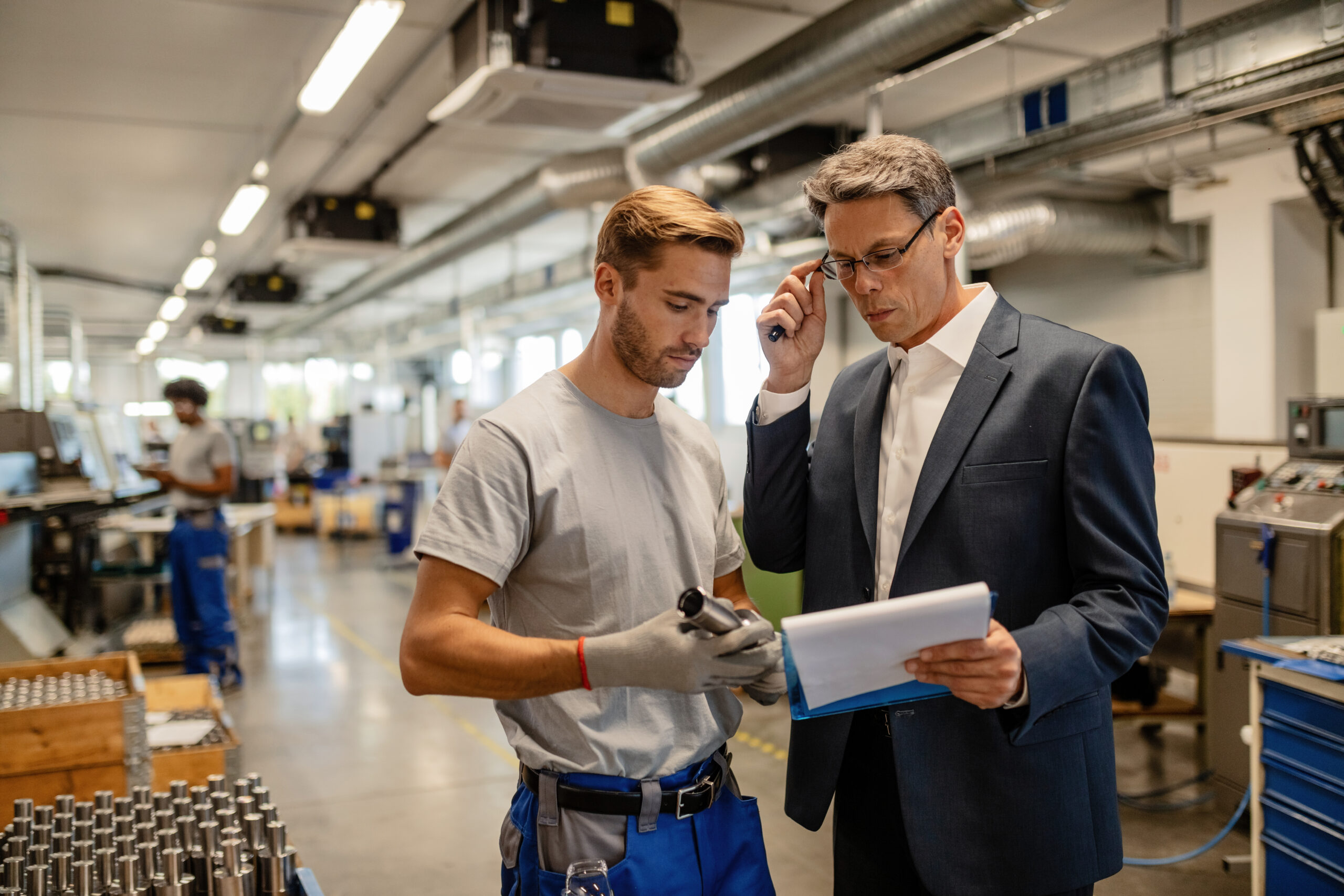 Quality control inspector and metal worker reading reports in industrial building